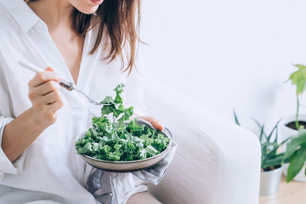 woman in white dress holding silver fork and knife slicing green vegetable on white ceramic bowl